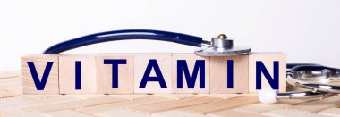 VITAMIN kelimesi ahşap bir arka planda steteskopun yanındaki tahta küplere yazılmıştır. Tıbbi konsept