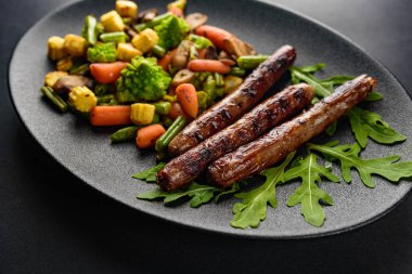 siyah bir tablo üzerinde siyah bir tabakta sebze ile ızgara sosis