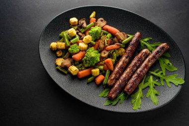 siyah bir tablo üzerinde siyah bir tabakta sebze ile ızgara sosis