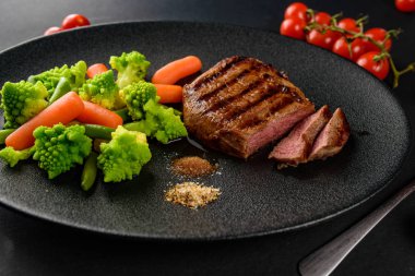 siyah bir tabakta sebze ile nadir sığır eti biftek orta bir parça kesip