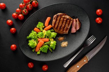 siyah bir tabakta sebze ile nadir sığır eti biftek orta bir parça kesip