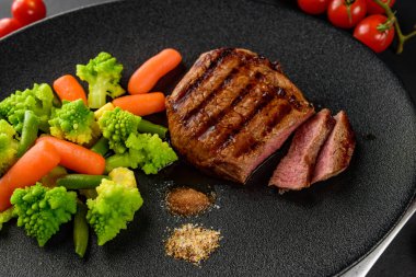 siyah bir tabakta sebze ile nadir sığır eti biftek orta bir parça kesip