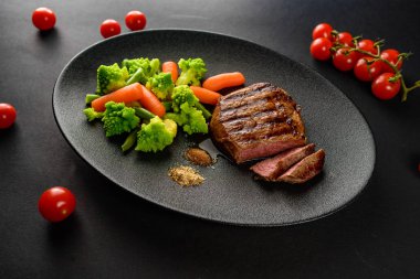 siyah bir tabakta sebze ile nadir sığır eti biftek orta bir parça kesip