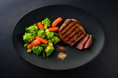 siyah bir tabakta sebze ile nadir sığır eti biftek orta bir parça kesip