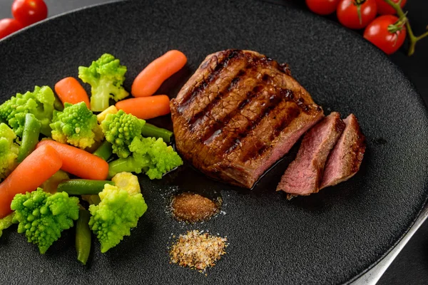 siyah bir tabakta sebze ile nadir sığır eti biftek orta bir parça kesip