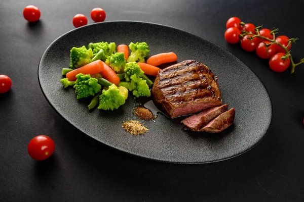 siyah bir tabakta sebze ile nadir sığır eti biftek orta bir parça kesip