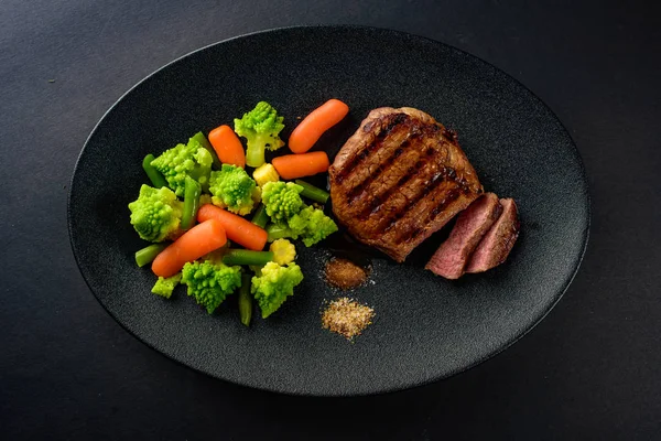 siyah bir tabakta sebze ile nadir sığır eti biftek orta bir parça kesip