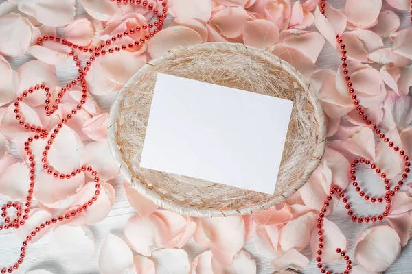 Pembe gül yapraklarından oluşan bir sepetin içinde boş bir kağıt parçası.