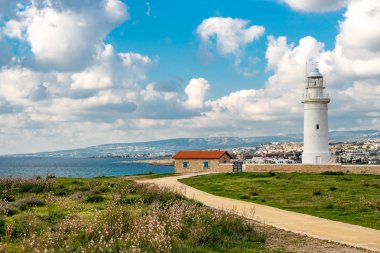 Pafos kentinin arka planına karşı Kıbrıs 'taki harabelerin yanında beyaz deniz feneri