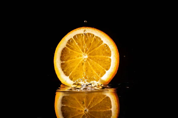 sulu turuncu dilim yansıması ile siyah bir arka plan üzerinde sıçramaları ile suya düşüyor