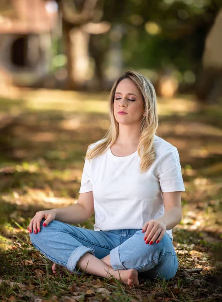 Güzel genç bir kadın parkta meditasyon yapıyor, açık havada ve ağaçların altında.