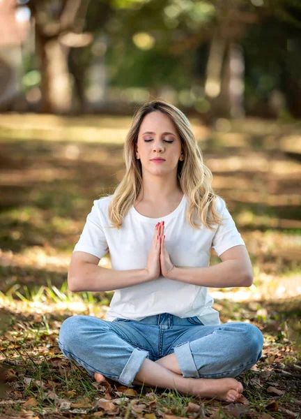 Güzel genç bir kadın parkta meditasyon yapıyor, açık havada ve ağaçların altında.