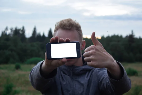 Happy man showing a blank mobile phone screen outdoor with a green background