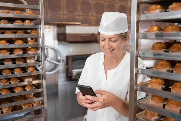 Baker woman smiling and texting with her phone surrounded by cupcakes