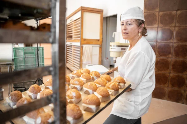 Baker woman putting a cupcake tray on a shelve with a wooden shovel