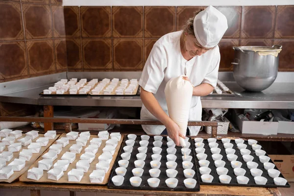 Fırıncı kadın kek hazırlamak için hamur işini hamur torbasıyla kalıba döküyor.