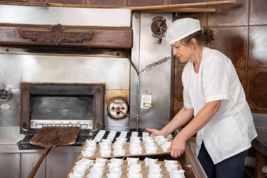 Fırıncı kadın fırının yanındaki kek tepsilerini düzenliyor.