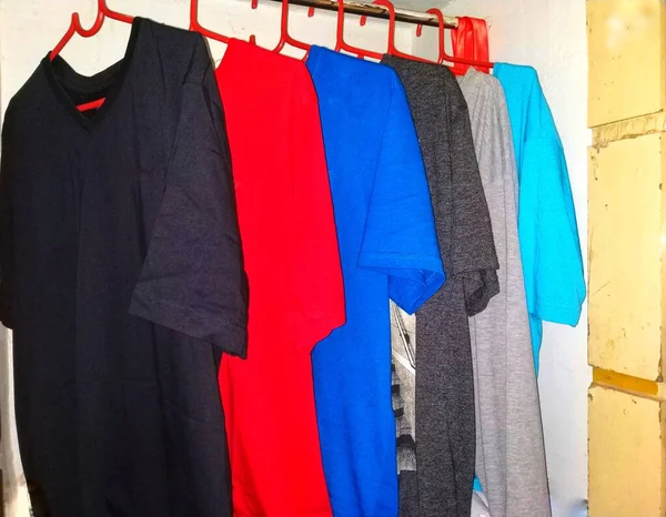 不同颜色的T恤衫分别挂在橱柜里 有红色衣架的黑色 银色和浅蓝色T恤 — 图库照片