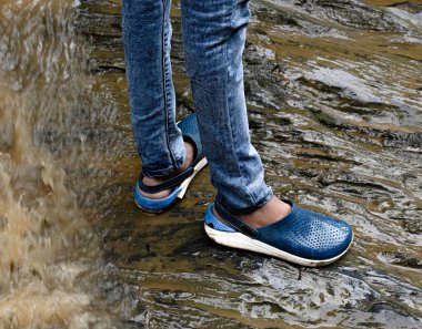 Human legs safely standing on a wet rock surface ,water flowing behind in the city of yellapur, Karnataka/India - 08/13/2020 clipart