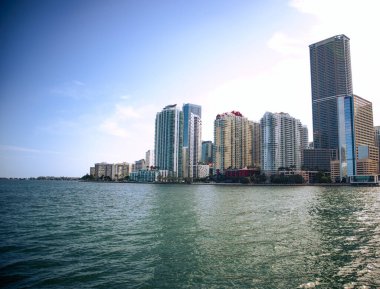 Brickell, Miami, Florida 'daki binaların sıcak görünüşü, gökdelenlerin aksine Miami' deki bir şehrin sıcak görüntüsü, yüksek doğuşların ve güneşin suda yansıması, sıcaklık, güneşli, mavi gökyüzü, beyaz bulutlar, şehir., 