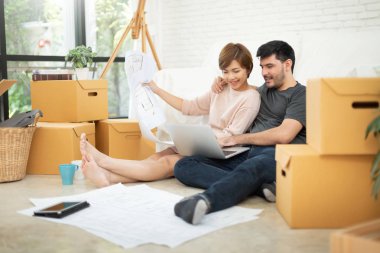 Dizüstü bilgisayar ve onların yeni ev taşıma planlama planları ile mutlu genç çift. Birbirimizi gülümseyen.