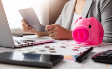 Hesabı hesap cüzdanı tutan kadın vurguladı. Hesap makinesi, pembe kumbara, dizüstü bilgisayar, iş grafik ve grafik belge üstünde okul sırası. Borç.