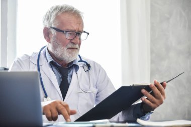 Üst düzey erkek doktor düşünme ve bir panosuna bir hastanede hasta tıbbi kayıtlarını kontrol. Tıbbi ve sağlık kavramı. Vurguladı. Konsantrasyon.