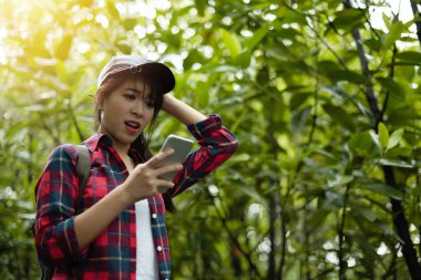 Asyalı kız Gezgini kullanarak dijital harita ile smartphone yeşil doğal zemin üzerine kırmızı ekose gömlekli. Endişeli, gergin.