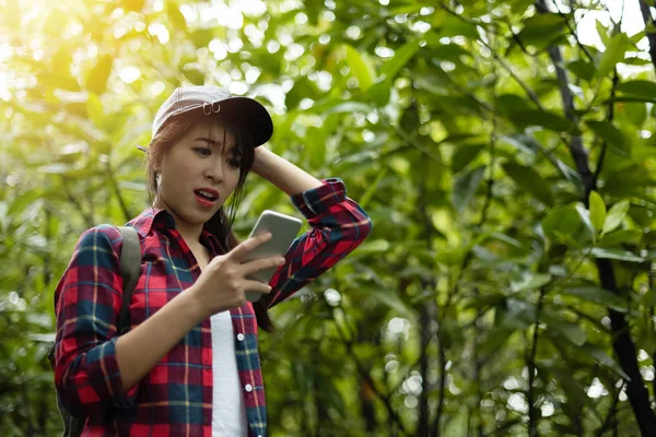 Asyalı kız Gezgini kullanarak dijital harita ile smartphone yeşil doğal zemin üzerine kırmızı ekose gömlekli. Endişeli, gergin.