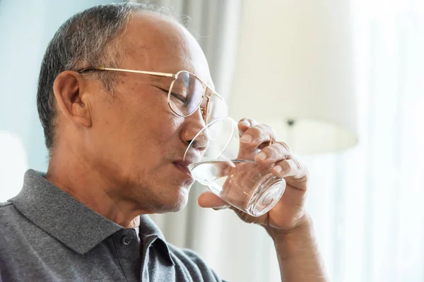 Asian Senior man drinking water. Elderly male holding transparent glass in his hand.