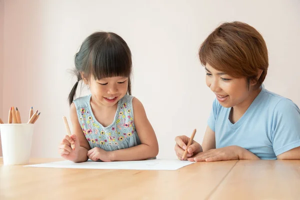 Happy Asian Mother and daughter drawing together. Kid and her teacher having Fun in kindergarten.
