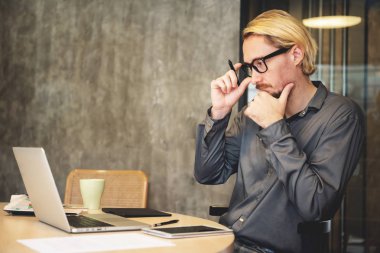 Oturma ve ofiste dizüstü bilgisayar ile yeni projeler için yeni fikirler düşünüyorum konsantre erkek Tasarımcısı giyim gözlük.