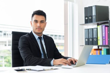 Ofiste odasında dizüstü bilgisayar üzerinde çalışan kendine güvenen bir işadamı portresi. Kamera için arıyorsunuz.