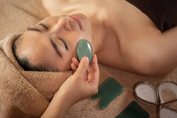 Güzel Asyalı kadın Spa Salon de yeşim yüz tedavi görüyor. Masöz ellerini yüzüne masaj yapıyor.