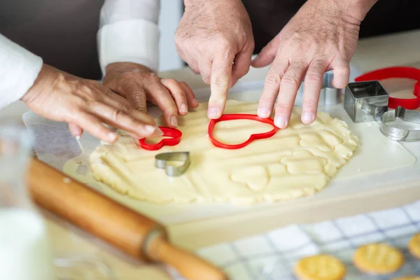 Close up Elderly Hands are making cookies with red cutters in heart shape.