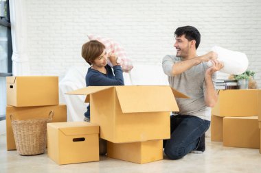 Mutlu genç çift yeni evde karton kutuları açma sırasında yastıklar holding ile eğleniyor. Ev taşıma.