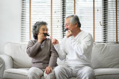 Kıdemli Çift kanepede oturuyor ve kağıt bıyık oynuyor.