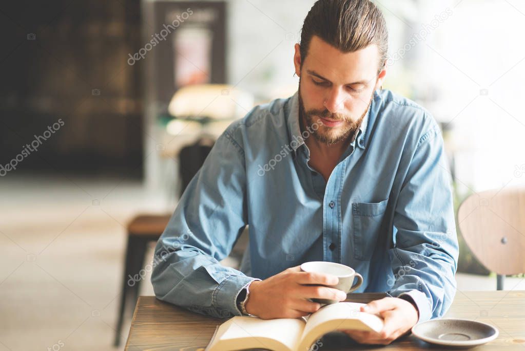 Male freelancer in blue shirt reading a book.