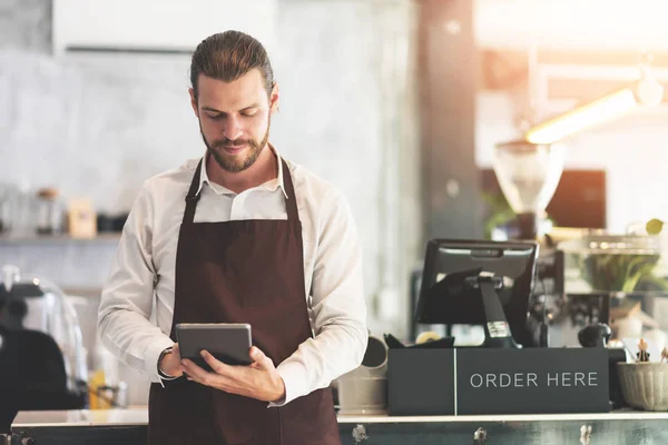 Männlicher Barista hält und schaut auf digitales Tablet. — Stockfoto