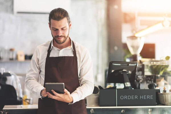 Male barista holding and looking at digital tablet.