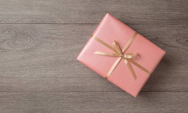 Ahşap arka planda altın kurdeleli pembe hediye kutusu.
