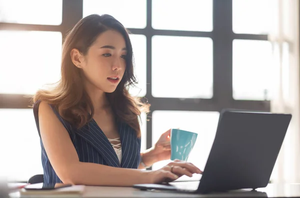 Jovem asiática do sexo feminino sentado e usando computador portátil no offi — Fotografia de Stock