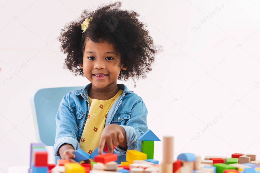 Little afro girl smiling and playing colorful wooden toys.