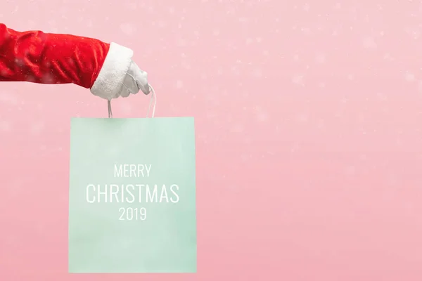 Santa Claus hand holding blue shopping bag on isolated pink back