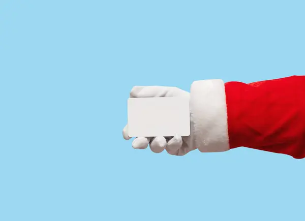 Santa Claus mano celebración de tarjeta de crédito de plástico sobre azul aislado —  Fotos de Stock