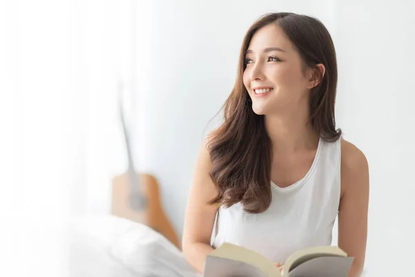 漂亮迷人的年轻女人坐在那里微笑着看着外面的卧室 在家里享受美丽的女性 快乐的亚洲女孩在白色的房间里看书 健康的生活方式 — 图库照片