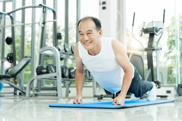 Sporty Asian Senior man in white shirt push up while exercising at the gym. Happy smiling Healthy Old male stretching after a workout. Sport, Recreation, Good health.