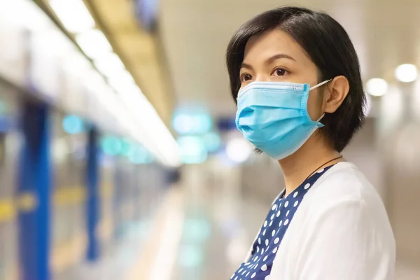 Asian Woman in face mask looking away and waiting commuter train or metro for traveling to work. Young female in public transportation while pandemic virus. Healthcare in New normal