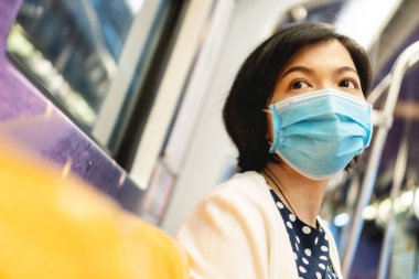 Koronavirüs ya da covid-19 için koruyucu maskeli güzel bir Asyalı kadın ya da banliyö treninde ya da metroda hava kirliliği. Genç bir bayan işe yeraltından gidiyor. Yeni normallerle.