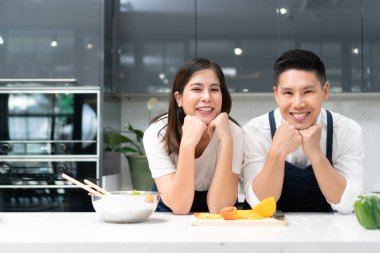 Mutlu Gülümseyen Şirin Adam 'ın portresi ve elleri çenesinde modern mutfakta kameraya bakan güzel bir kadın. Sağlıklı Asyalı çift aile hayatı evde aşkla eğleniyor.